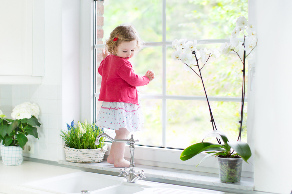 Cute toddler girl in a red dress watching out a window