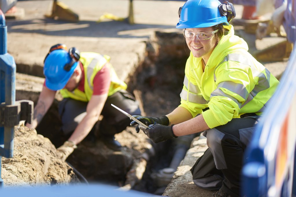 female gas engineer holds a new gas valve as she and a colleague prepare to replace the old pipework in a residential uk street .