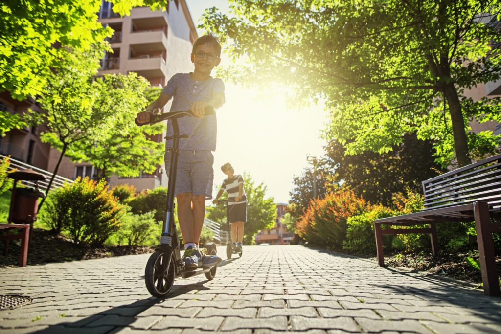 Kids riding scooters in city residential area.