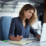 young businesswoman making notes while working on a laptop in a modern office