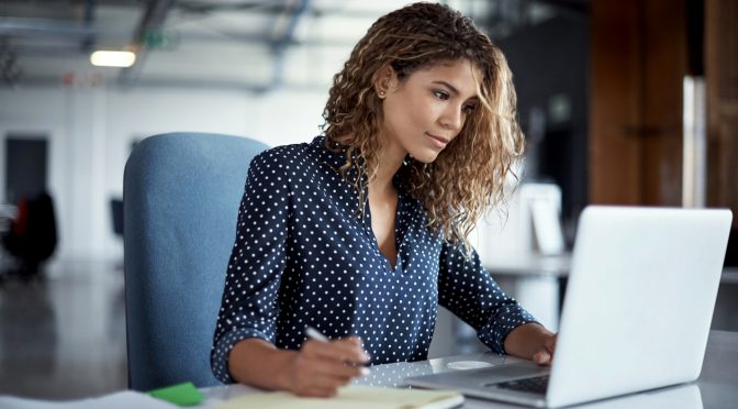 young businesswoman making notes while working on a laptop in a modern office