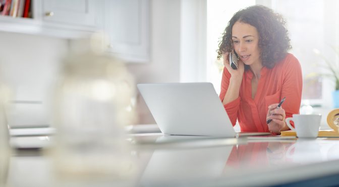 a woman in her kitchen paying a bill by phone