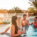 Group of happy friends making a pool party at sunset - Millennial young people laughing and having fun drinking champagne in the pool - Friendship, holidays and summer youth lifestyle concept