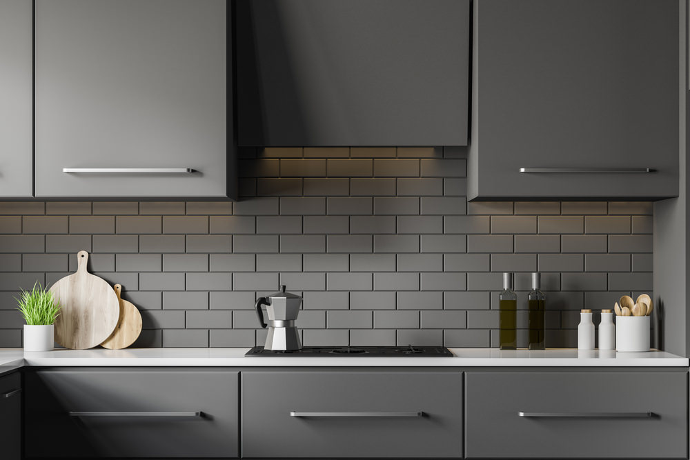 Interior of modern kitchen with grey brick walls, gray countertops with built in cooker and dark gray cupboards. 3d rendering