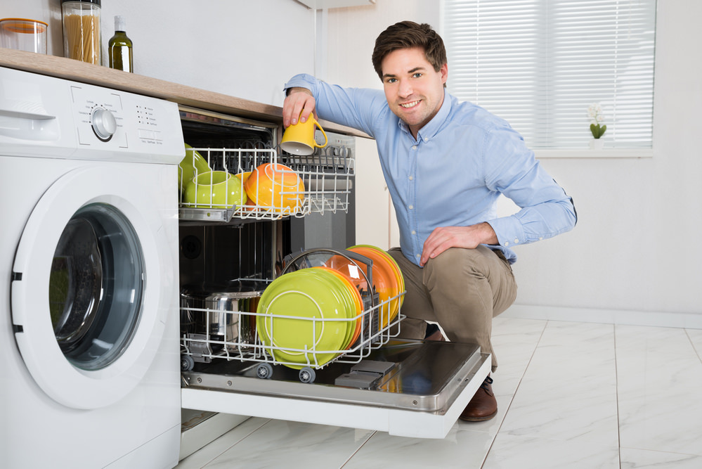 Young Happy Man Arranging Dishes In Dishwasher In Modern Kitchen