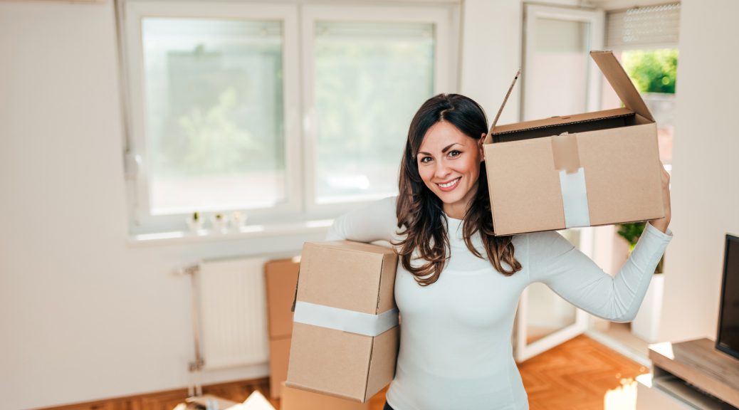 Lovely casual young woman holding cardboard boxes and looking at camera.