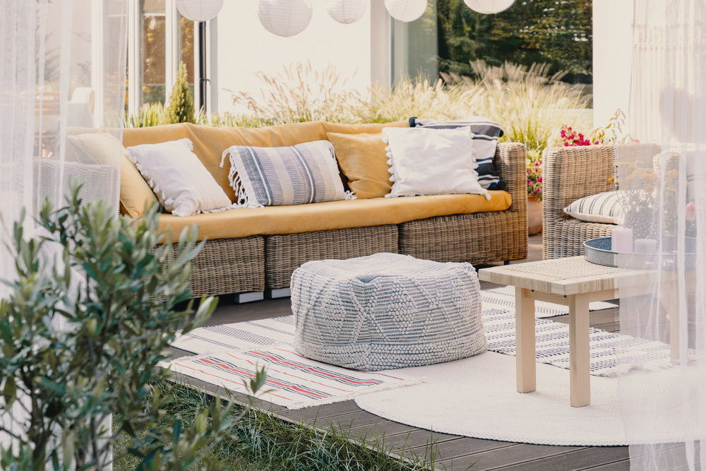 Stylish outdoor relax area with garden furniture and comfortable pouf, real photo